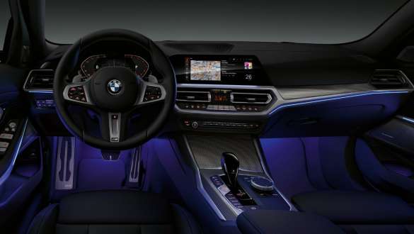 Luz ambiente do BMW Série 3 Sedan (G20). Visão frontal da cabine do motorista do BMW Série 3 Sedan (G20) com espaço iluminado para as pernas com uma luz ambiente azul.