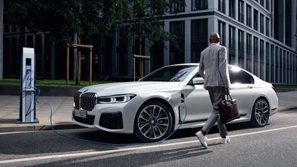 Vista lateral 3/4 do modelo híbrido plug-in BMW Série 7 Sedan G11 G12 sendo recarregado Vista lateral 3/4 do modelo híbrido plug-in BMW Série 7 Sedan G11 G12 sendo recarregado, ao lado de uma modelo
