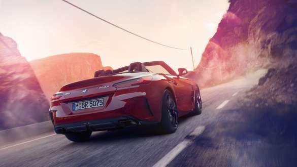 BMW Z4 Roadster 2020 vermelho realizando curva no asfalto em meio a montanhas, visão traseira de três quartos BMW Z4 Roadster 2020 vermelho realizando curva no asfalto em meio a montanhas, visão traseira de três quartos