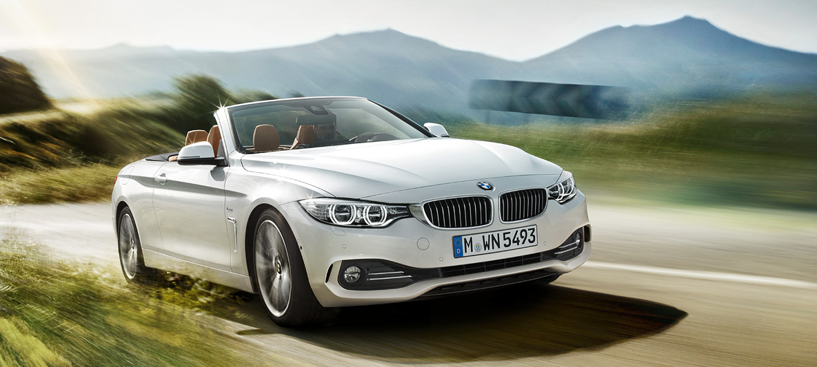 Vista aproximada do BMW Série 4 430i Cabrio na cor prata alpine viajando na estrada ensolarada, visão frontal direita de três quartos Vista aproximada do BMW Série 4 430i Cabrio na cor prata alpine viajando na estrada ensolarada, visão frontal direita de três quartos