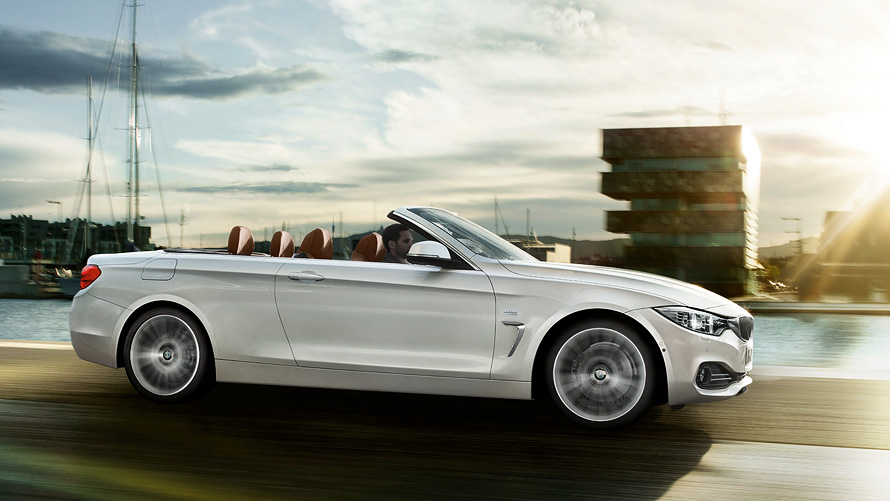 Visão lateral do BMW 430i Cabrio em cor prata Alpine trafegando por uma estrada ensolarada Visão lateral do BMW 430i Cabrio em cor prata Alpine trafegando por uma estrada ensolarada