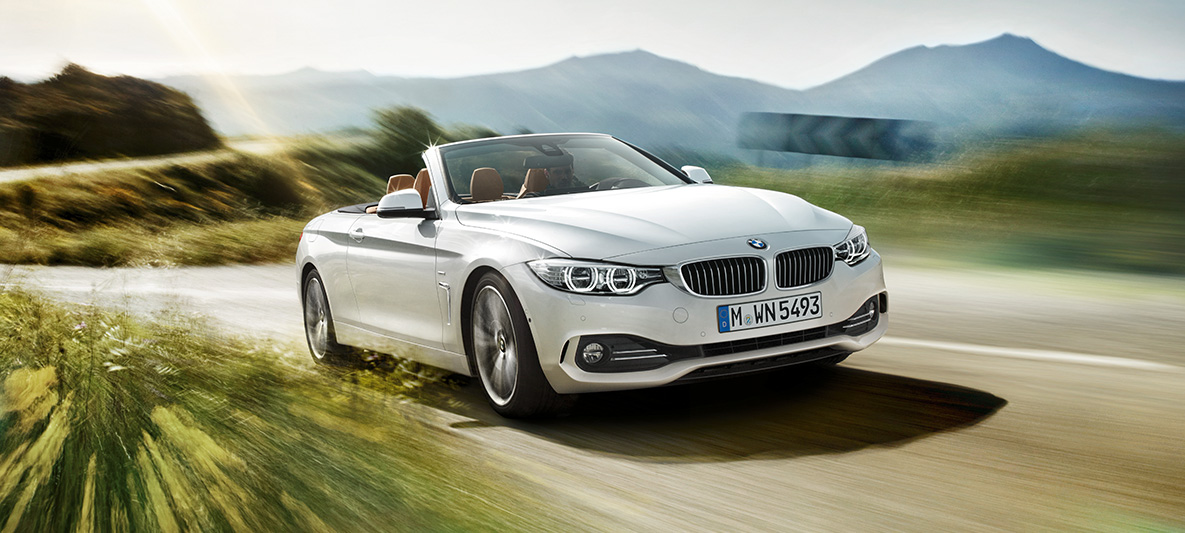 BMW Série 4 430i Cabrio na cor prata alpine andando na estrada em dia de sol, visão frontal esquerda de três quartos BMW Série 4 430i Cabrio na cor prata alpine andando na estrada em dia de sol, visão frontal esquerda de três quartos