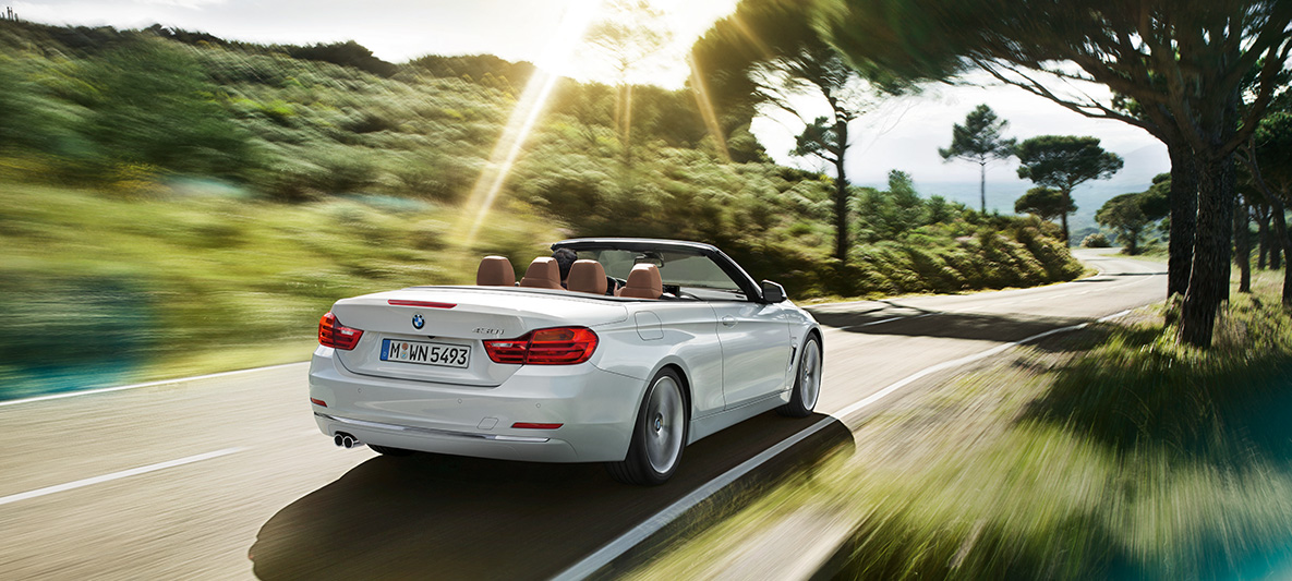 BMW Série 4 430i Cabrio na cor prata alpine andando na estrada em dia de sol, visão traseira de três quartos BMW Série 4 430i Cabrio na cor prata alpine andando na estrada em dia de sol, visão traseira de três quartos