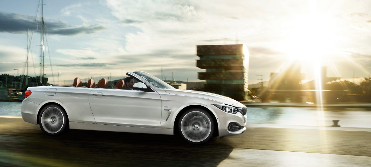 Visão lateral do BMW 430i Cabrio em cor prata Alpine trafegando por uma estrada ensolarada Visão lateral do BMW 430i Cabrio em cor prata Alpine trafegando por uma estrada ensolarada