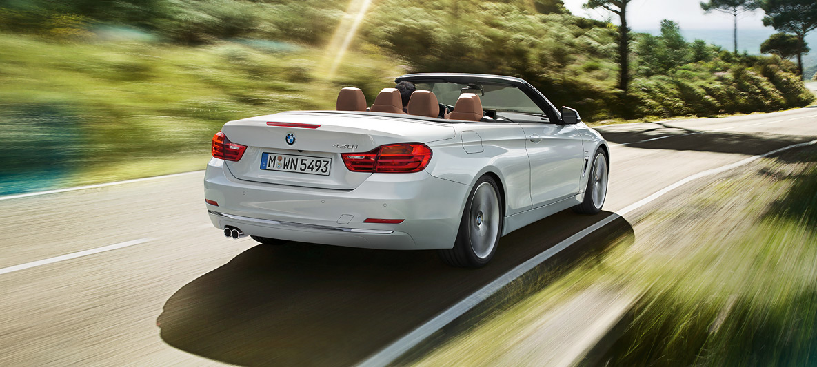 BMW Série 4 430i Cabrio na cor prata alpine andando na estrada em dia de sol, visão traseira de três quartos BMW Série 4 430i Cabrio na cor prata alpine andando na estrada em dia de sol, visão traseira de três quartos