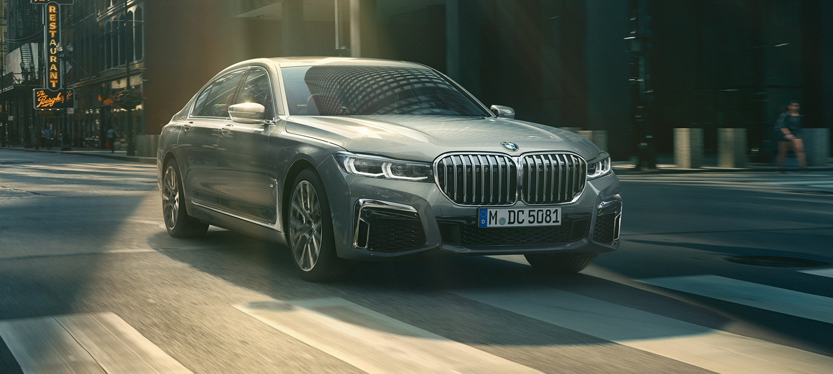 O BMW Série 7 Sedan na tonalidade Grey vista frontal 3/4 O BMW Série 7 Sedan na tonalidade Grey atravessa um panorama urbano, nesta vista frontal 3/4