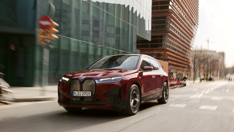 Assistente do motorista no SUV elétrico BMW iX i20 e no BMW iX xDrive50 SUV elétrico BMW iX i20 2021 e o BMW iX xDrive50 na tonalidade Aventurin Red dirigindo em um ambiente urbano