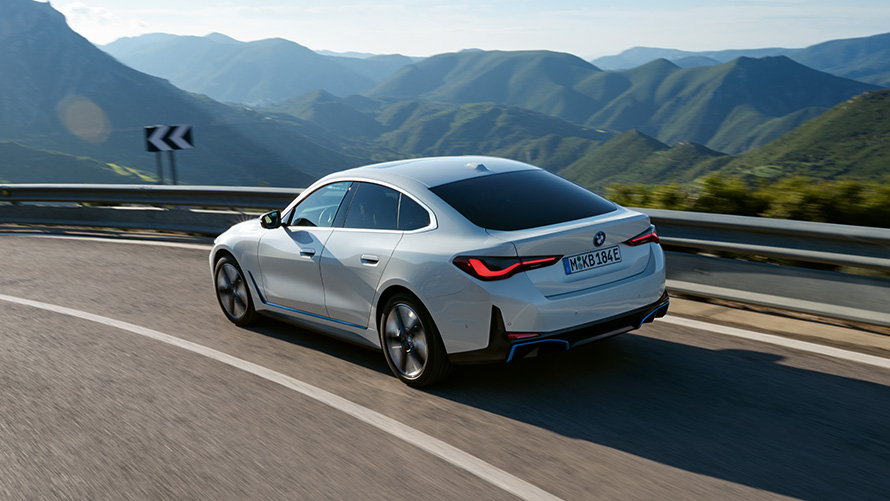 Vista traseira 3/4, BMW i4 eDrive40 G26, em movimento. BMW i4 eDrive40 G26, pintura Mineral White, vista traseira 3/4, em movimento.