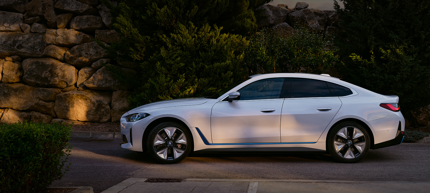 Vista dianteira 3/4 do BMW i4 eDrive40 G26 , pintura Mineral White, em frente a um lago, com uma montanha ao fundo.