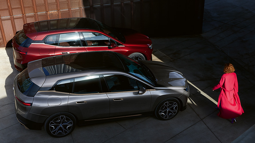 BMW iX M60 BMW Individual Storm Bay metallic e BMW iX xDrive50 Aventurin Red i20 visão de longe.