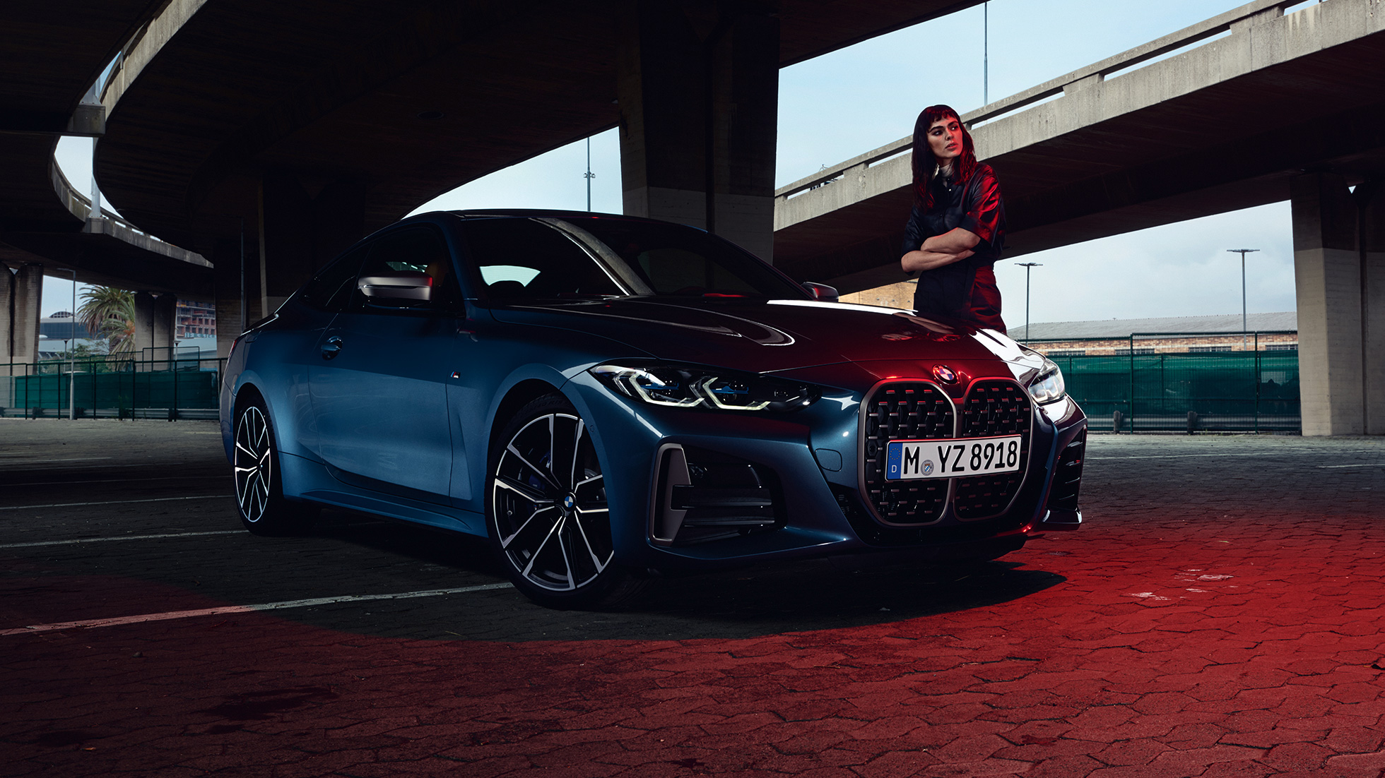 Vista lateral 3/4 do BMW M440i xDrive Coupé, G22, 2020, com uma modelo ao lado Vista lateral 3/4 do BMW M440i xDrive Coupé, exterior na tonalidade Arctic Race Blue metálico, G22, 2020, com uma modelo