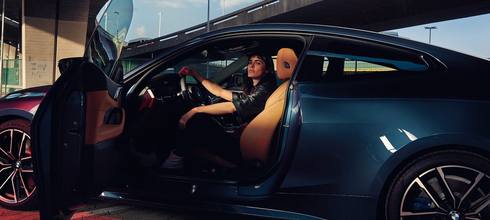 Vista lateral do BMW M440i xDrive Coupé, G22, 2020, com uma modelo Vista lateral do BMW M440i xDrive Coupé G22, 2020 com exterior na tonalidade Arctic Race Blue metálico, mostrando uma modelo no interior do automóvel, com a porta aberta