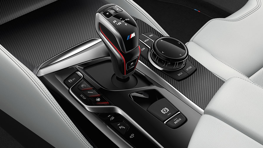 Manopla de Câmbio da BMW M5 2020 Sedã ao lado dos controles iDrive e de outras funções de condução, em cor preta e cinza metálico Manopla de Câmbio da BMW M5 2020 Sedã ao lado dos controles iDrive e de outras funções de condução, em cor preta e cinza metálico