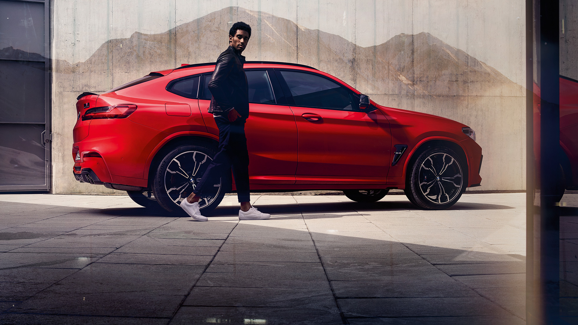 BMW X4 M Competition, visão lateral com um jovem. BMW X4 M Competition em vermelho metálico Toronto, exterior, visão lateral com um jovem.