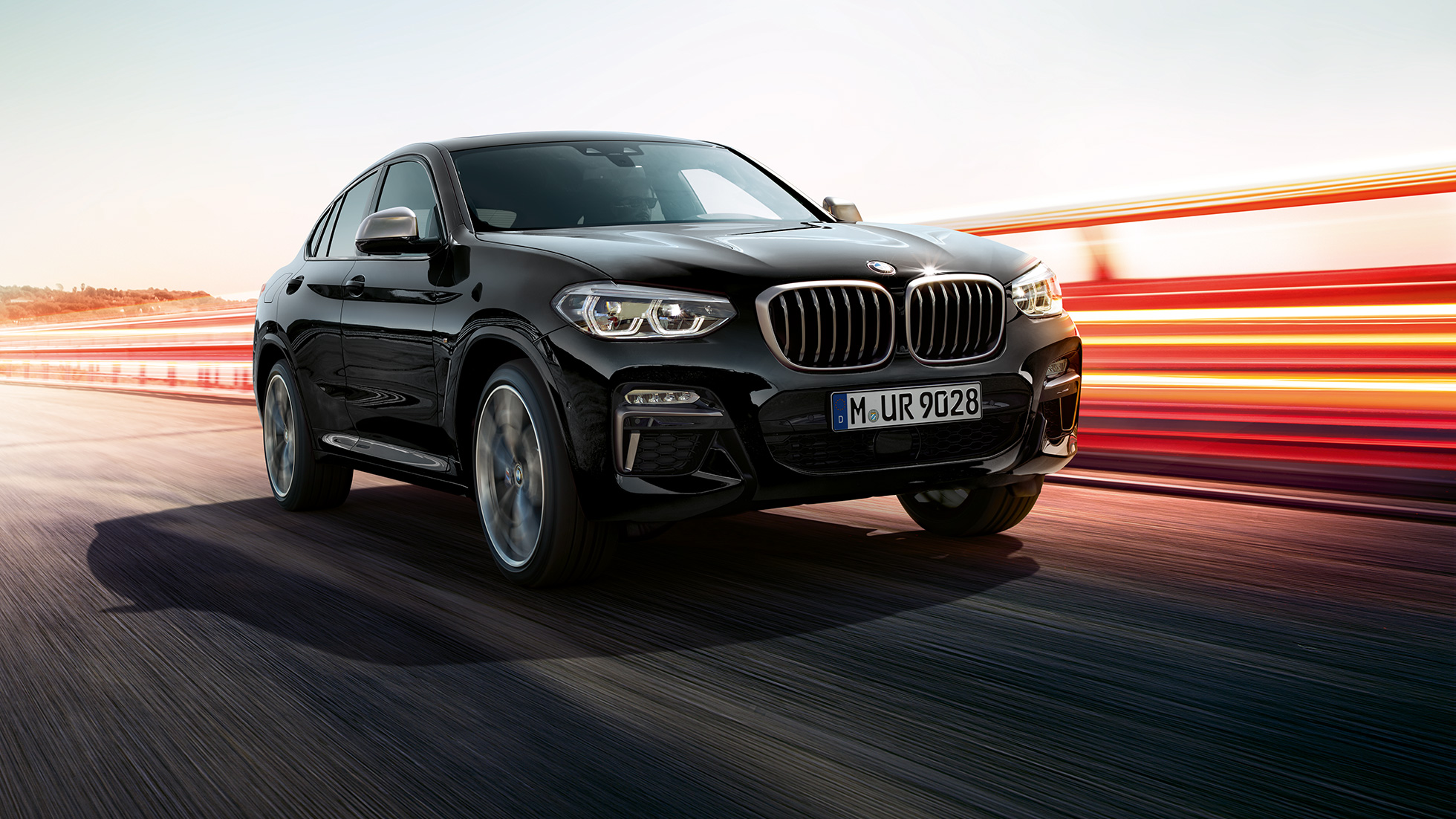 BMW X4 M40i e BMW X4 M40d, visão frontal de três quartos. BMW X4 M40i e BMW X4 M40d em preto safira metálico, exterior, visão frontal de três quartos, lado esquerdo com tiras de luz.