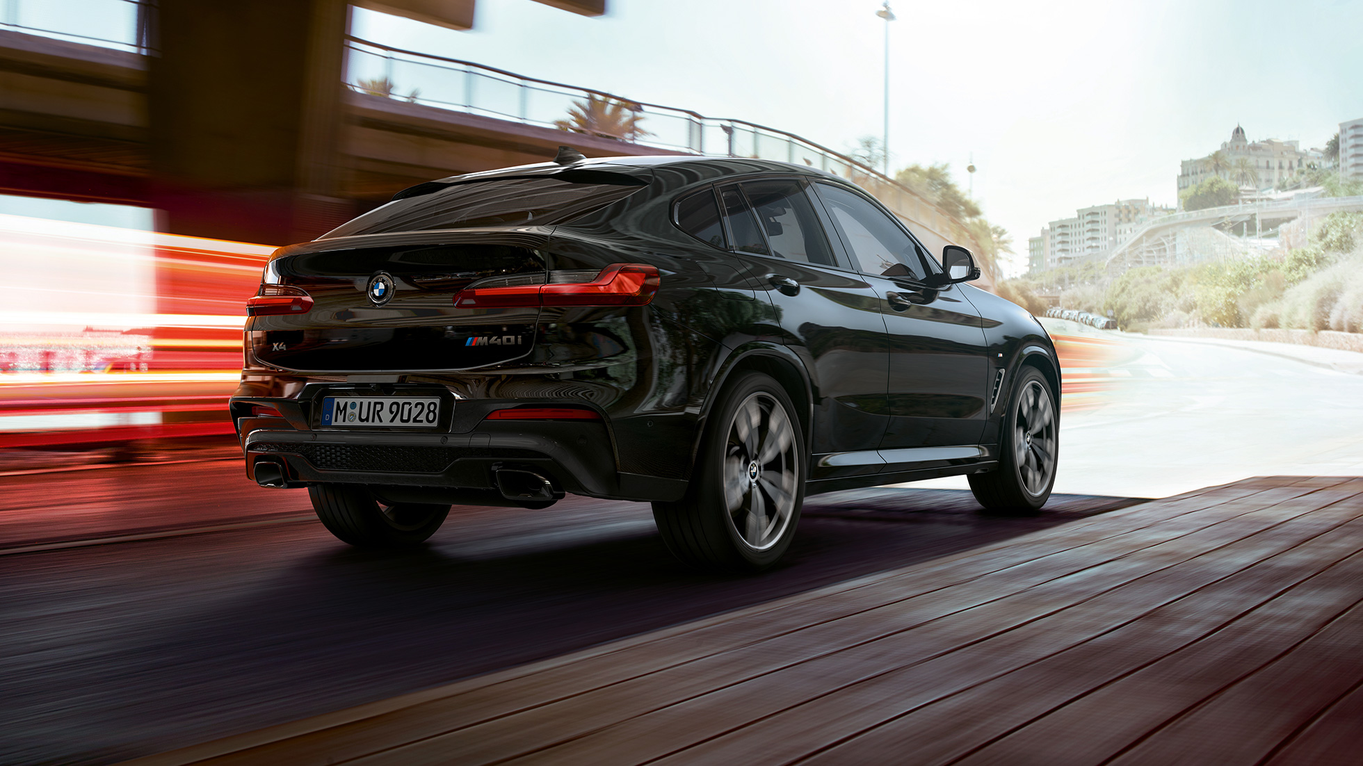 BMW X4 M40i, visão traseira de três quartos. BMW X4 M40i em preto safira metálico, exterior, visão traseira de três quartos, lado direito com tiras de luz.