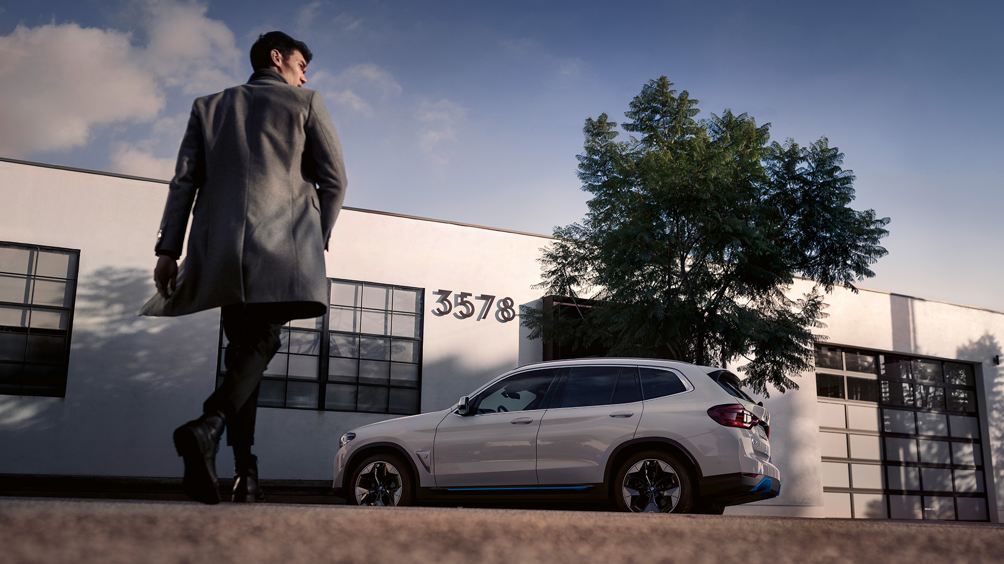 BMW iX3, G08, vista frontal em frente a um edifício com um homem BMW iX3, G08, 2020, cor exterior branco Mineral metalizada, vista frontal em frente a um edifício com um homem