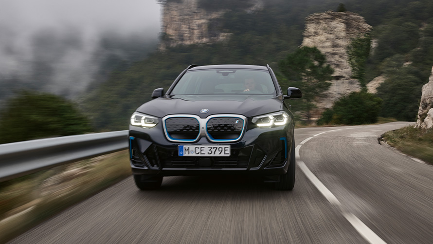 Vista frontal lateral do BMW iX3 em movimento na estrada.