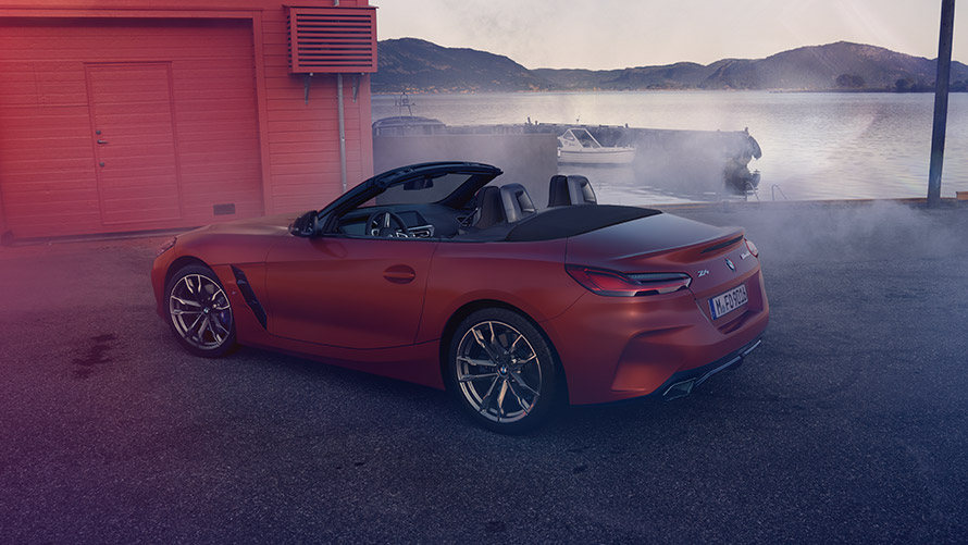 Vista traseira de um BMW Z4 First Edition laranja Vista traseira de um BMW Z4 First Edition na cor laranja à frente de uma casa vermelha na praia