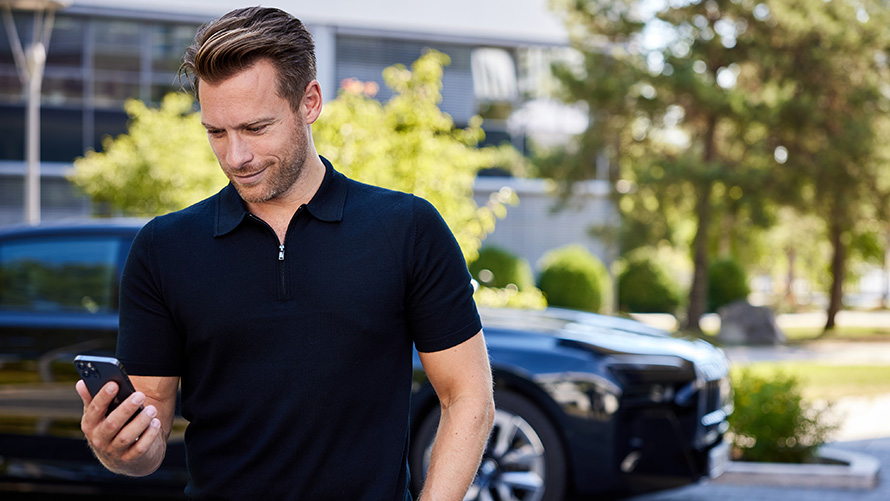 BMW Online Genius, homem em frente a um BMW. BMW Online Genius, homem com smartphone em frente a um BMW.