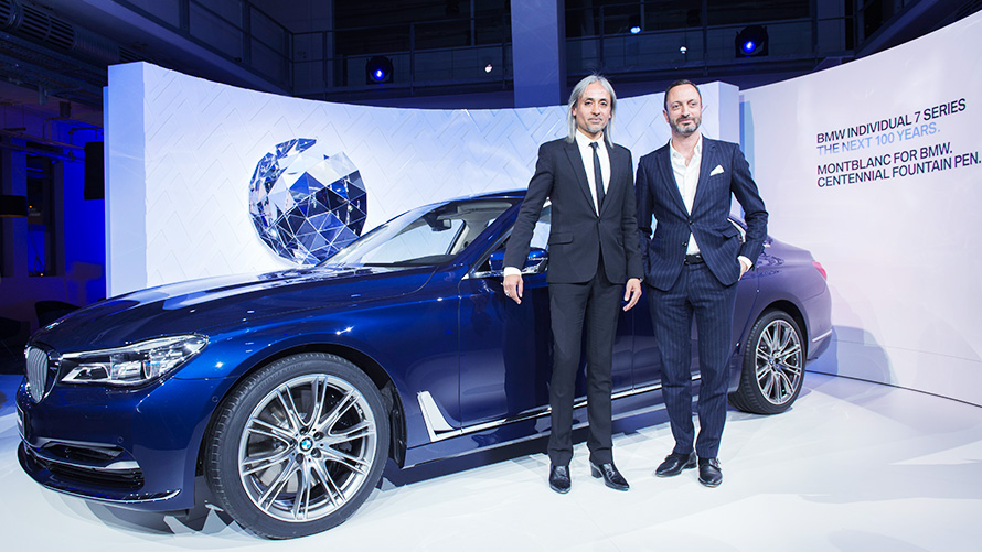 Dois apresentadores de terno ao lado do novo BMW Série 7 The Next 100 Years, em cor azul Dois apresentadores de terno ao lado do novo BMW Série 7 The Next 100 Years, em cor azul
