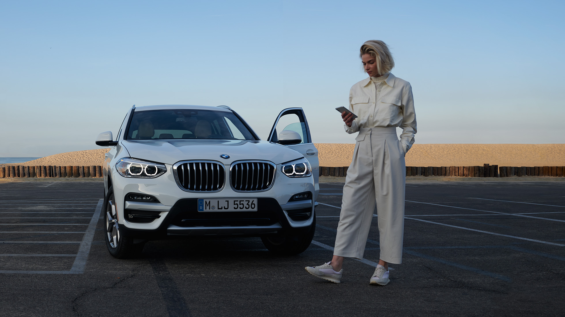 Mulher a utilizar a aplicação My BMW num smartphone Mulher a utilizar a aplicação My BMW através do BMW ConnectedDrive no smartphone em frente a um BMW X5 em branco