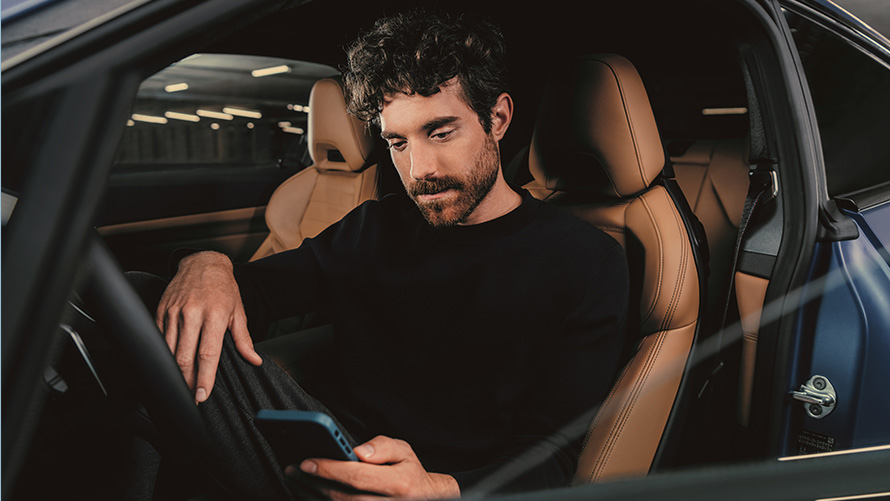 Um homem sentado em um BMW Um homem sentado em um BMW, olhando para o seu smartphone