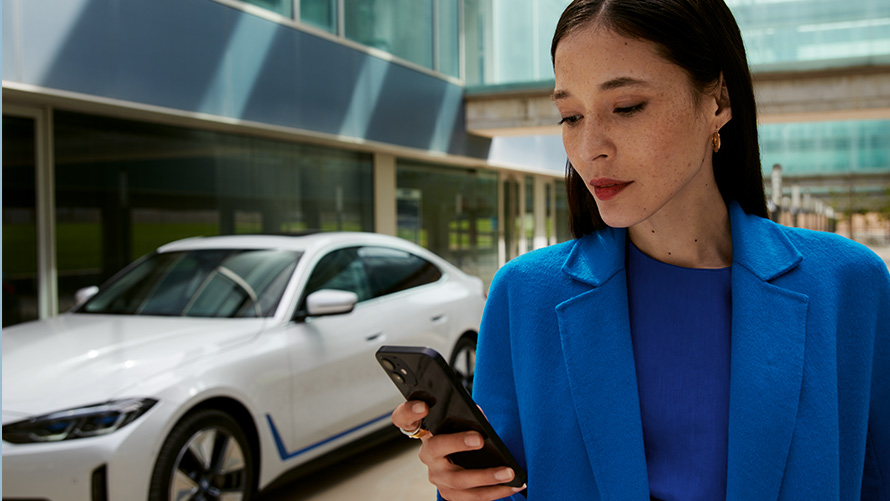 Uma mulher em frente a um BMW Uma mulher em frente a um BMW, olhando para o seu smartphone