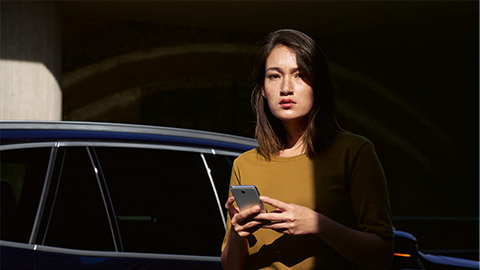 Visão geral do BMW ConnectedDrive BMW ConnectedDrive, serviços digitais, visão geral, mulher com smartphone em frente a um BMW