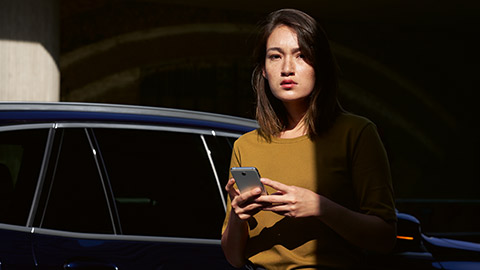 Visão geral do BMW ConnectedDrive, uma mulher com um smartphone em suas mãos, mostrando um BMW ao fundo