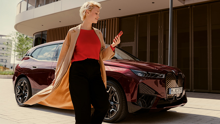 Aplicativo My BMW, mulher com um smartphone em frente a um BMW Mulher com um smartphone em frente a um BMW