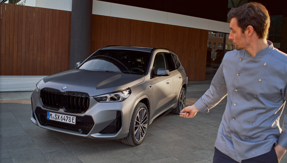 Homem inclinando-se sobre um BMW, em frente a um cenário de montanha Acessórios primavera/verão BMW, mostrando um homem inclinando-se sobre um BMW, em frente a um cenário de montanha
